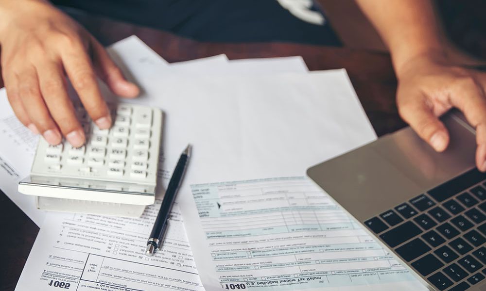Person using calculator and laptop for tax calculations on forms and documents.
