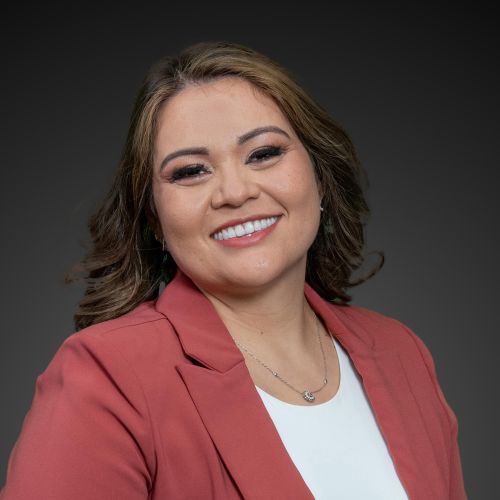 Smiling person in a red blazer against a dark background.