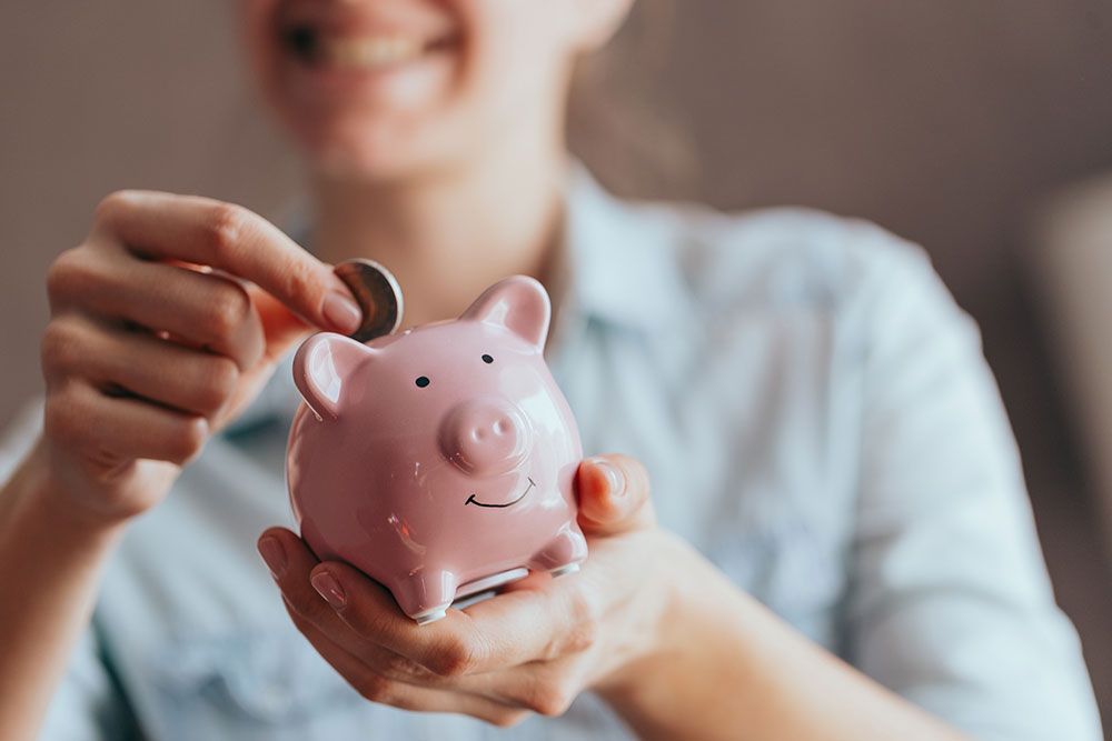 Smiling person saving money in a pink piggy bank, representing financial savings and budgeting.