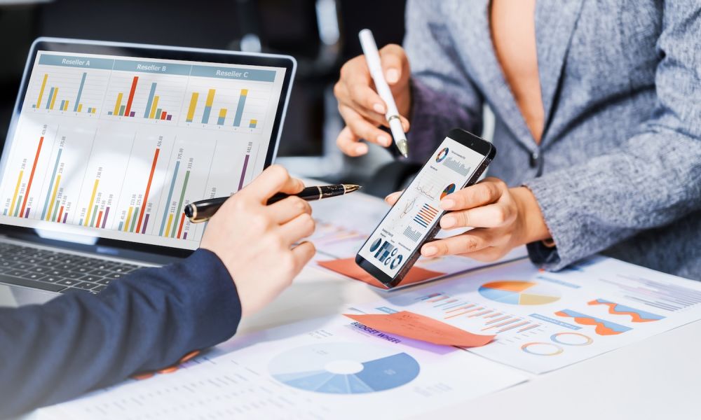 Business professionals reviewing data charts on laptop and smartphone during a meeting.