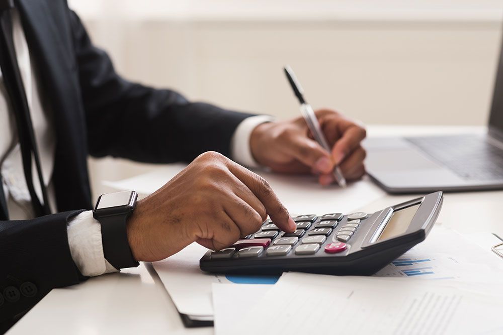 Person calculating finances with a calculator and laptop in an office setting, focusing on business documents.