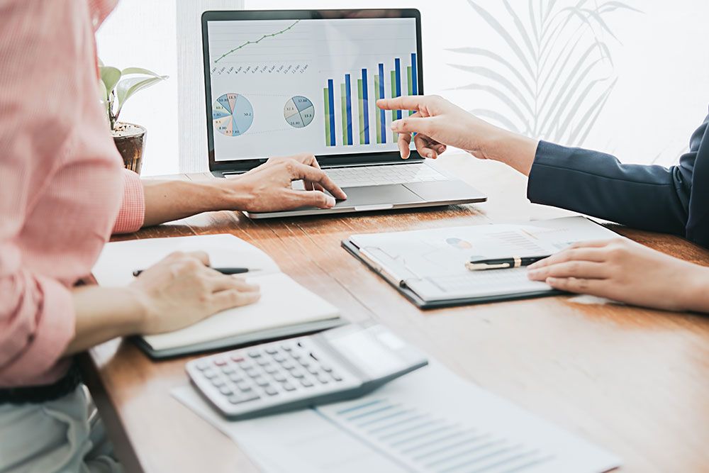 Business meeting with charts on laptop; professionals analyzing data and taking notes.