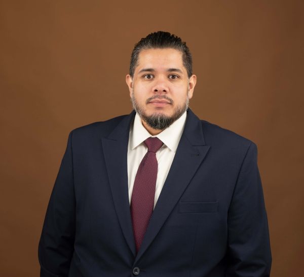 Juan Quintanilla in a suit and tie against a brown backdrop, looking into the camera.