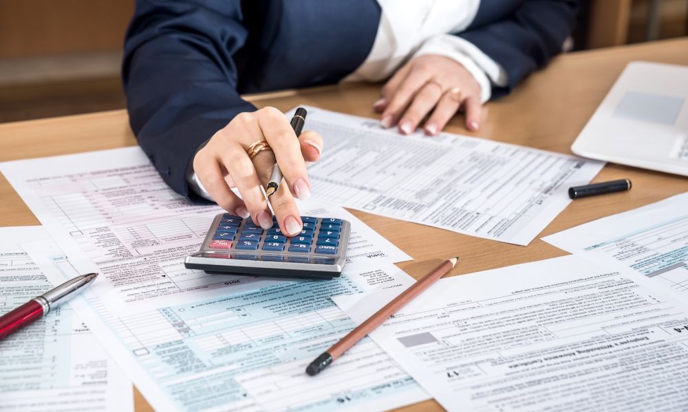Person using calculator on tax forms, financial paperwork, office desk.