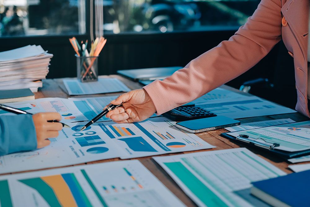 Two colleagues discussing financial charts and graphs in an office meeting with documents on the table.
