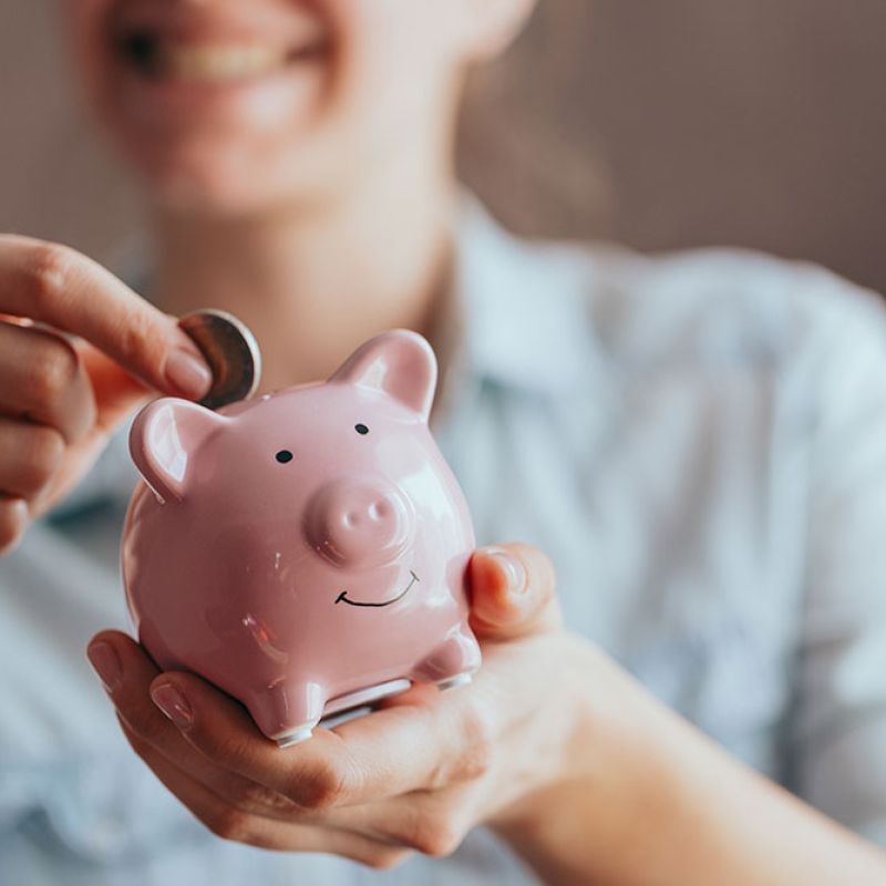 Smiling person saving money in a pink piggy bank, representing financial savings and budgeting.