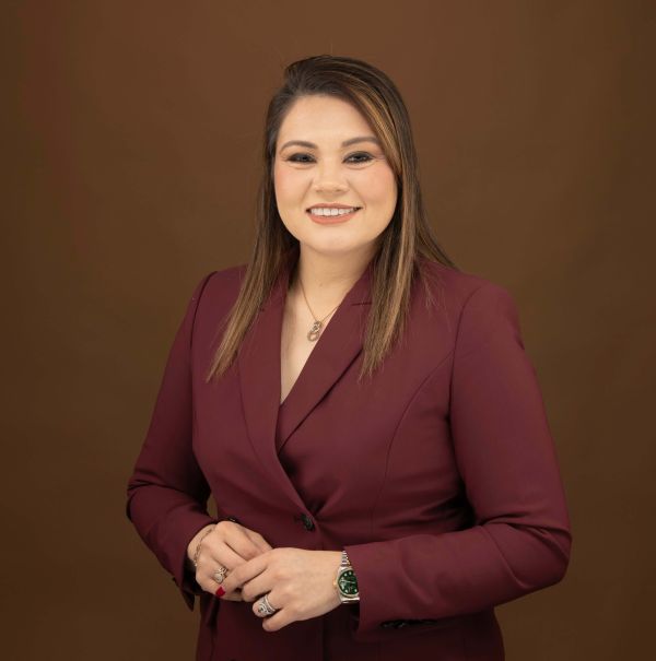 Karen Quintanilla in maroon blazer smiling against a brown background.