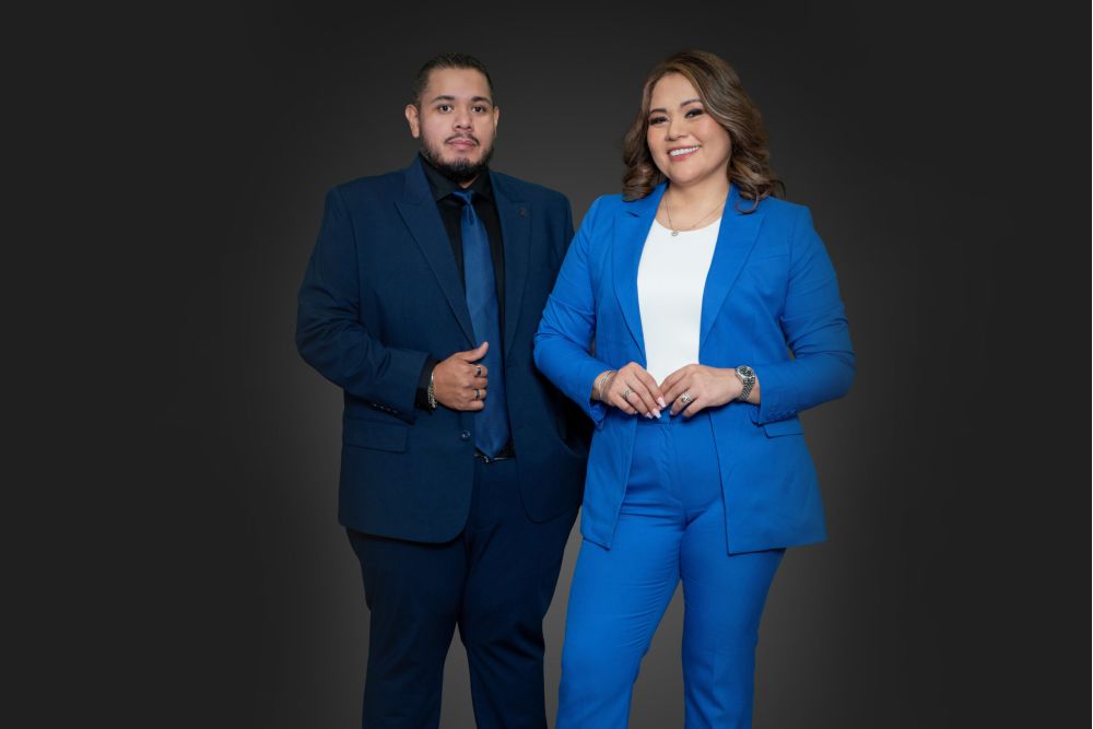 Two professionals in blue suits posing confidently against a dark background.