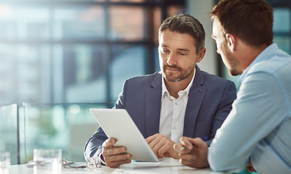 Two businessmen discussing over a tablet in a modern office setting.