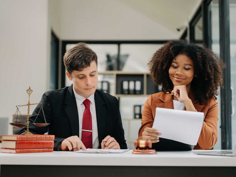 Lawyers reviewing paperwork at a table with a gavel and scales of justice in a modern office setting.