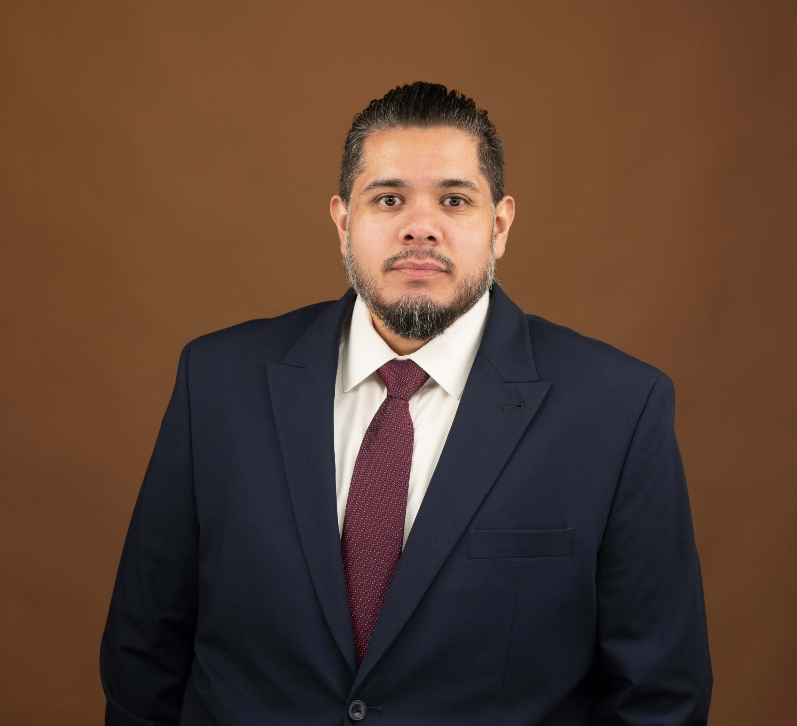 Juan Quintanilla in a suit and tie against a brown backdrop, looking into the camera.