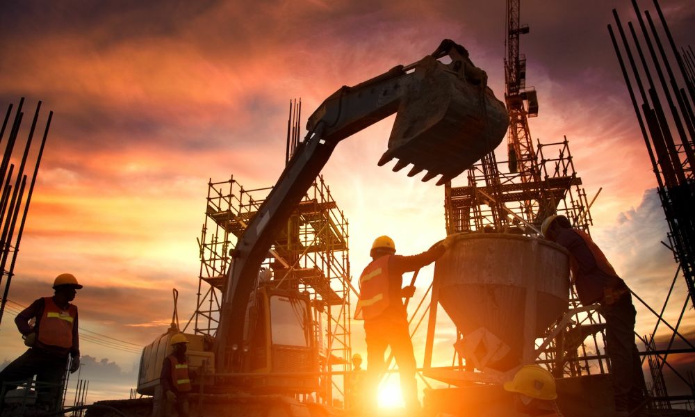 Construction workers at site during sunset, operating excavator and scaffolding equipment.