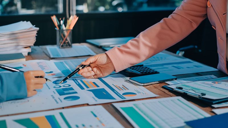 Two colleagues discussing financial charts and graphs in an office meeting with documents on the table.