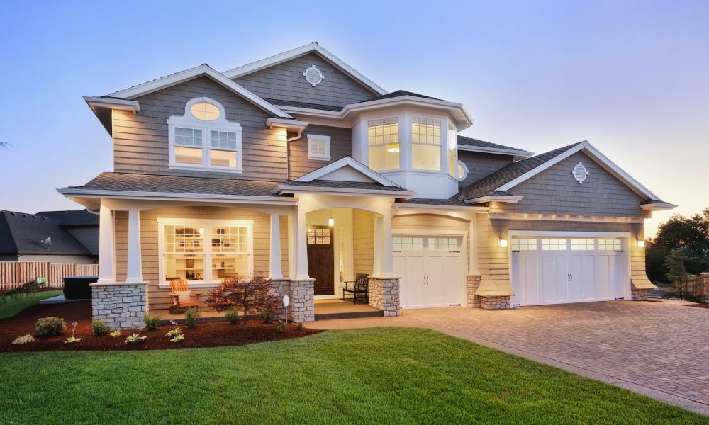Modern two-story house with landscaped yard, illuminated at dusk, featuring large windows and a spacious garage.