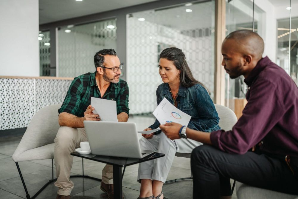 Team collaborating in modern office, discussing data charts on a laptop.