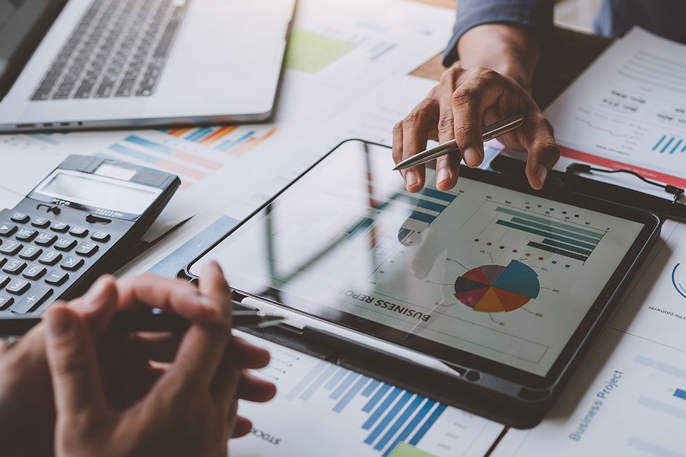 Business meeting analyzing charts on tablet and papers; laptop and calculator on table.