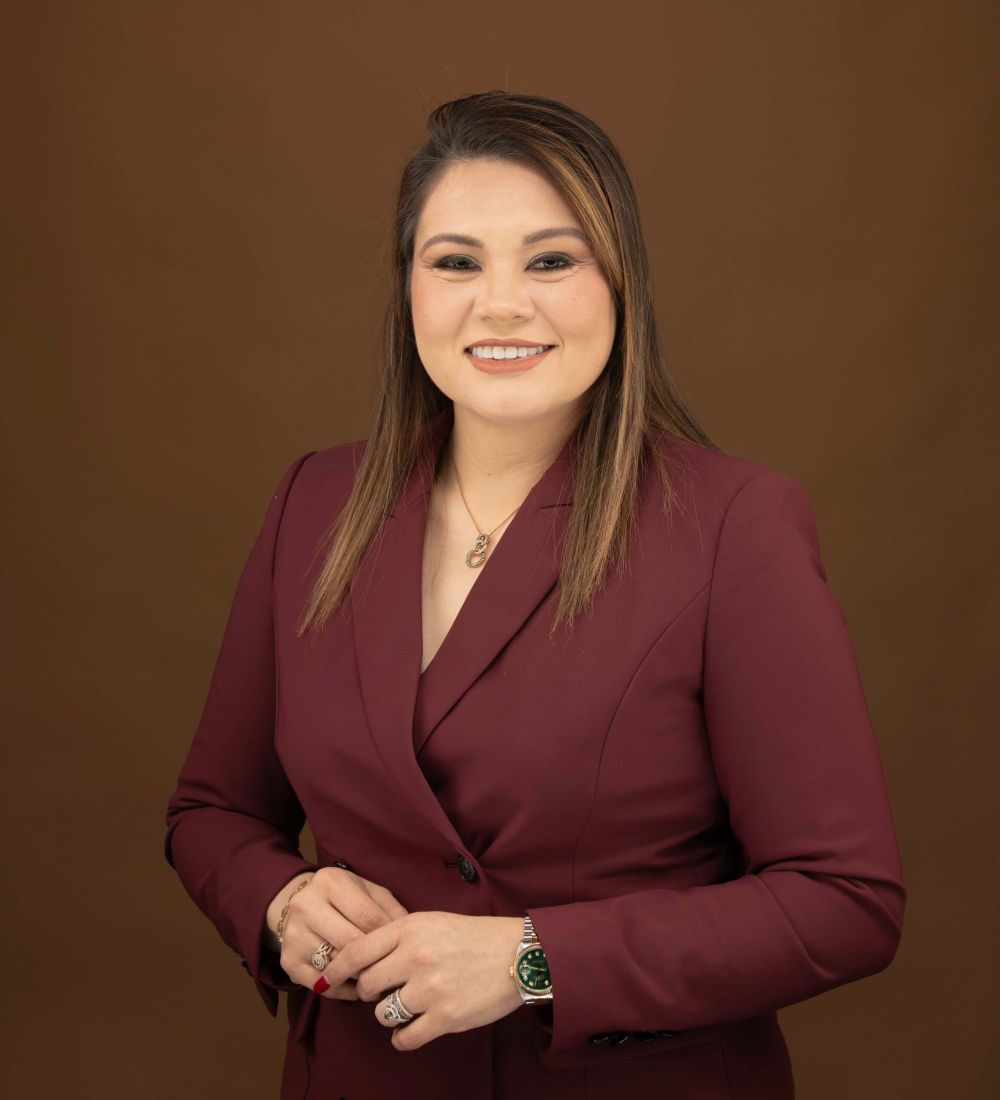 Karen Quintanilla in maroon blazer smiling against a brown background.