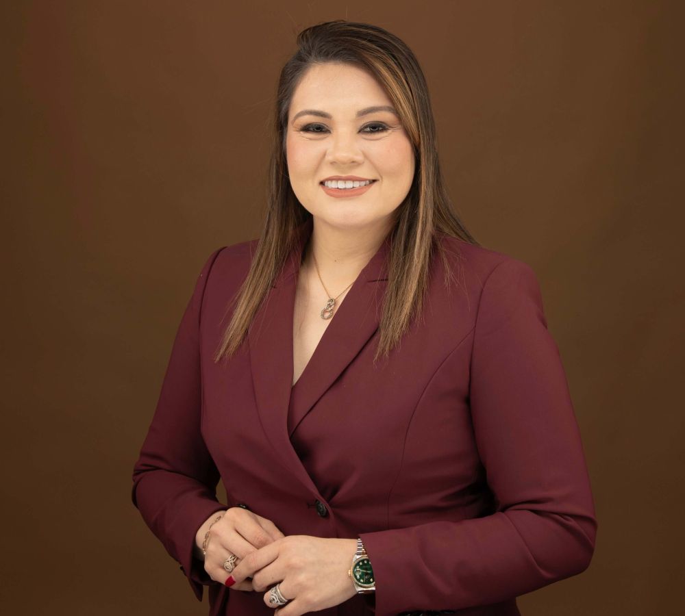 Karen Quintanilla in maroon blazer smiling against a brown background.