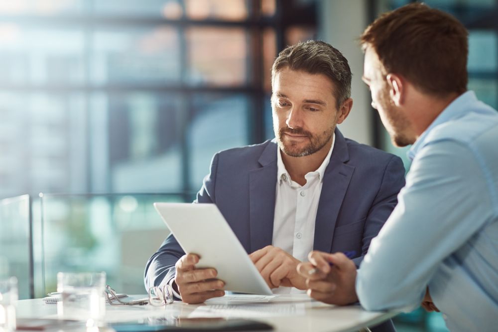 Two businessmen discussing over a tablet in a modern office setting.
