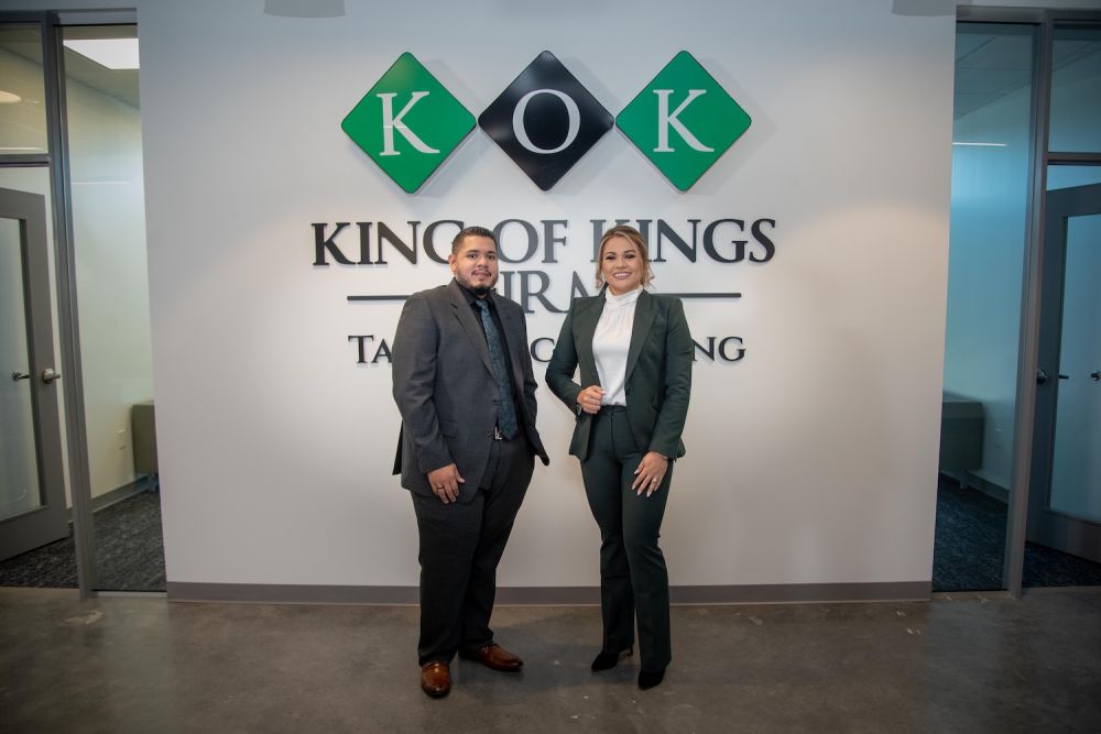 Two professionals pose in front of a King of Kings sign at a tax consulting firm office.