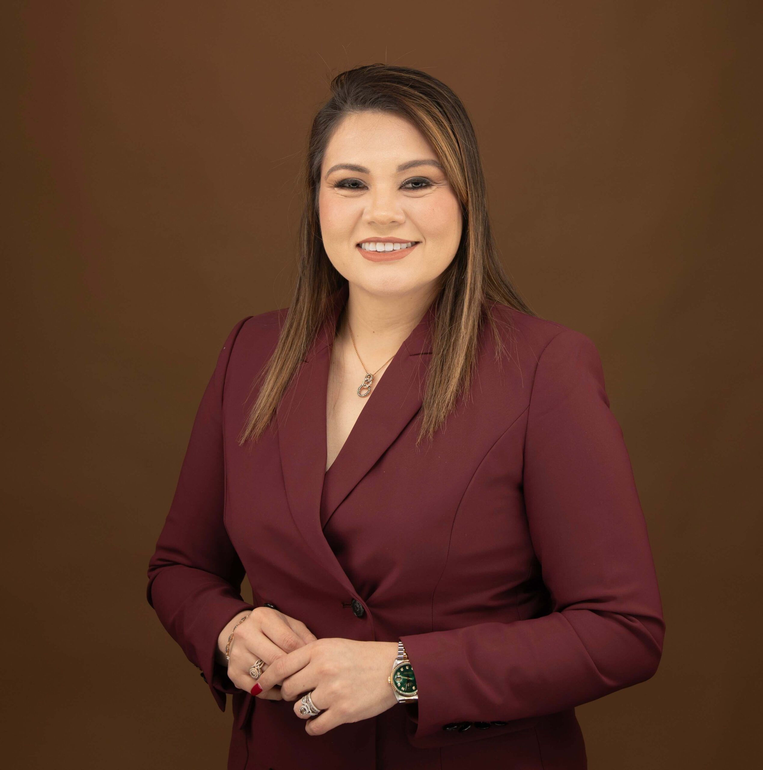 Karen Quintanilla in maroon blazer smiling against a brown background.