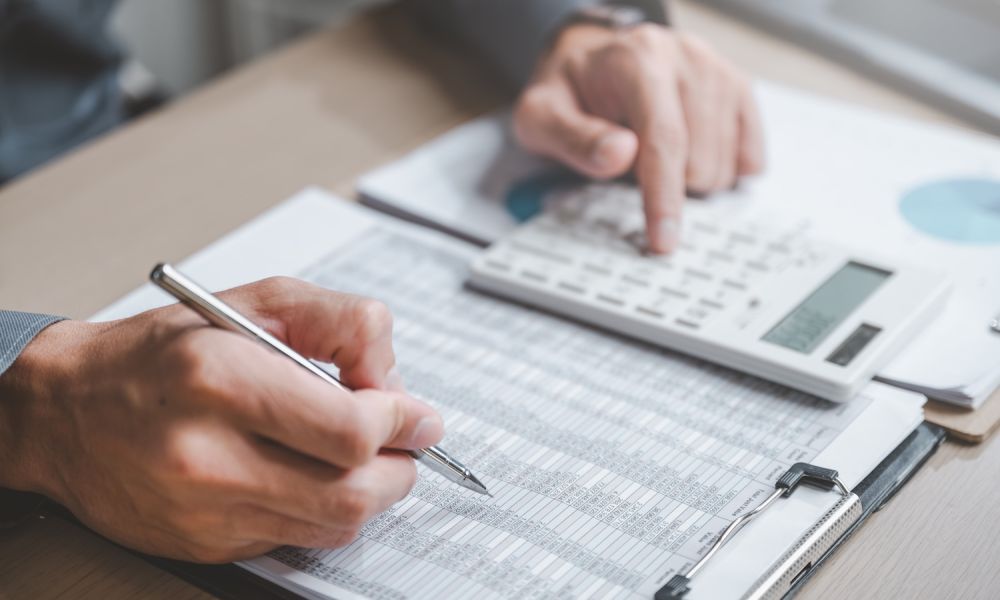 Person calculating financial data with a pen and a calculator at a desk.