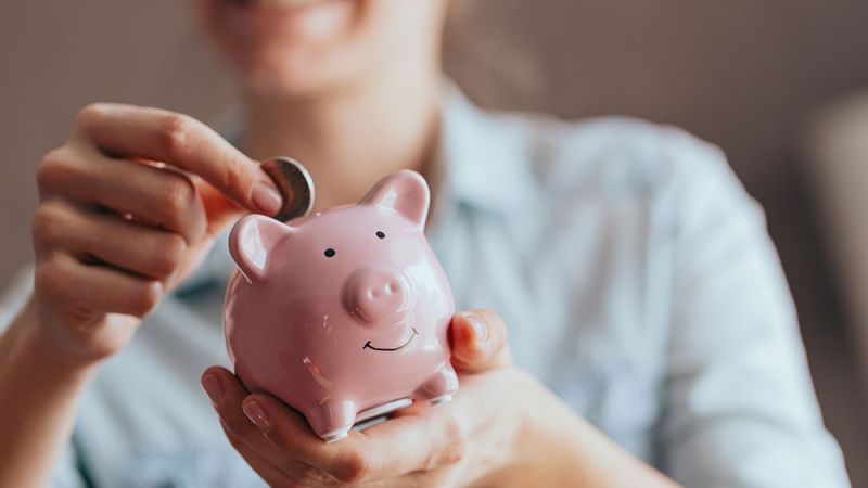 Smiling person saving money in a pink piggy bank, representing financial savings and budgeting.