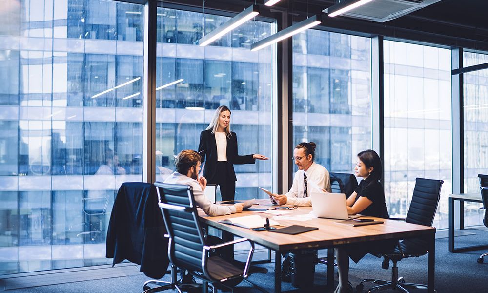 Business meeting in modern office with four professionals discussing documents around a conference table.
