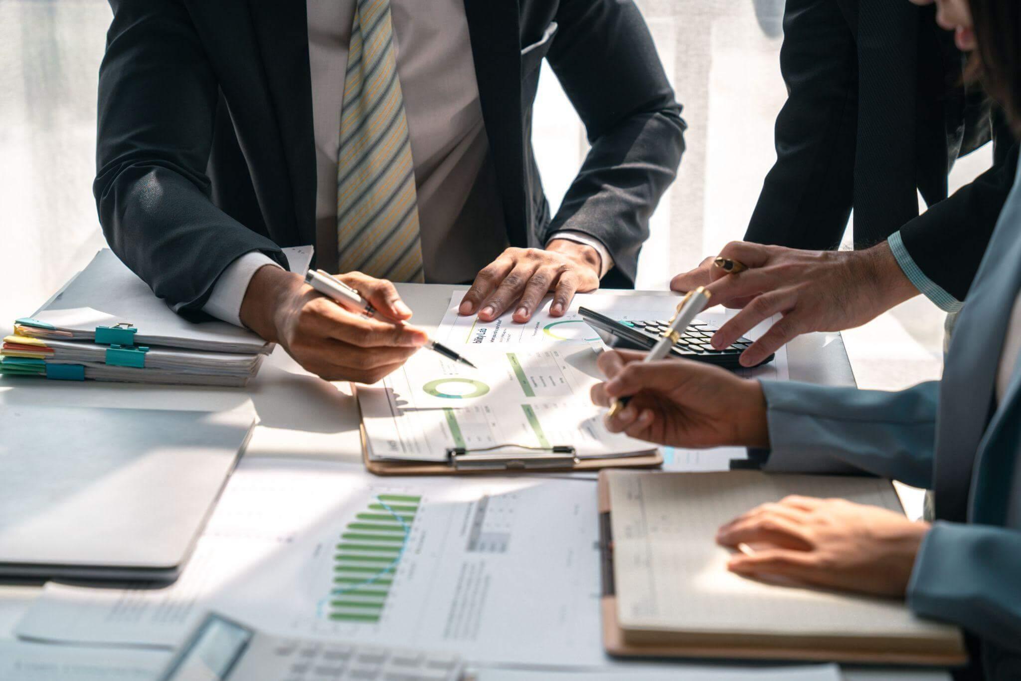 a group of businesspeople sitting around a table reviewing charts and numbers