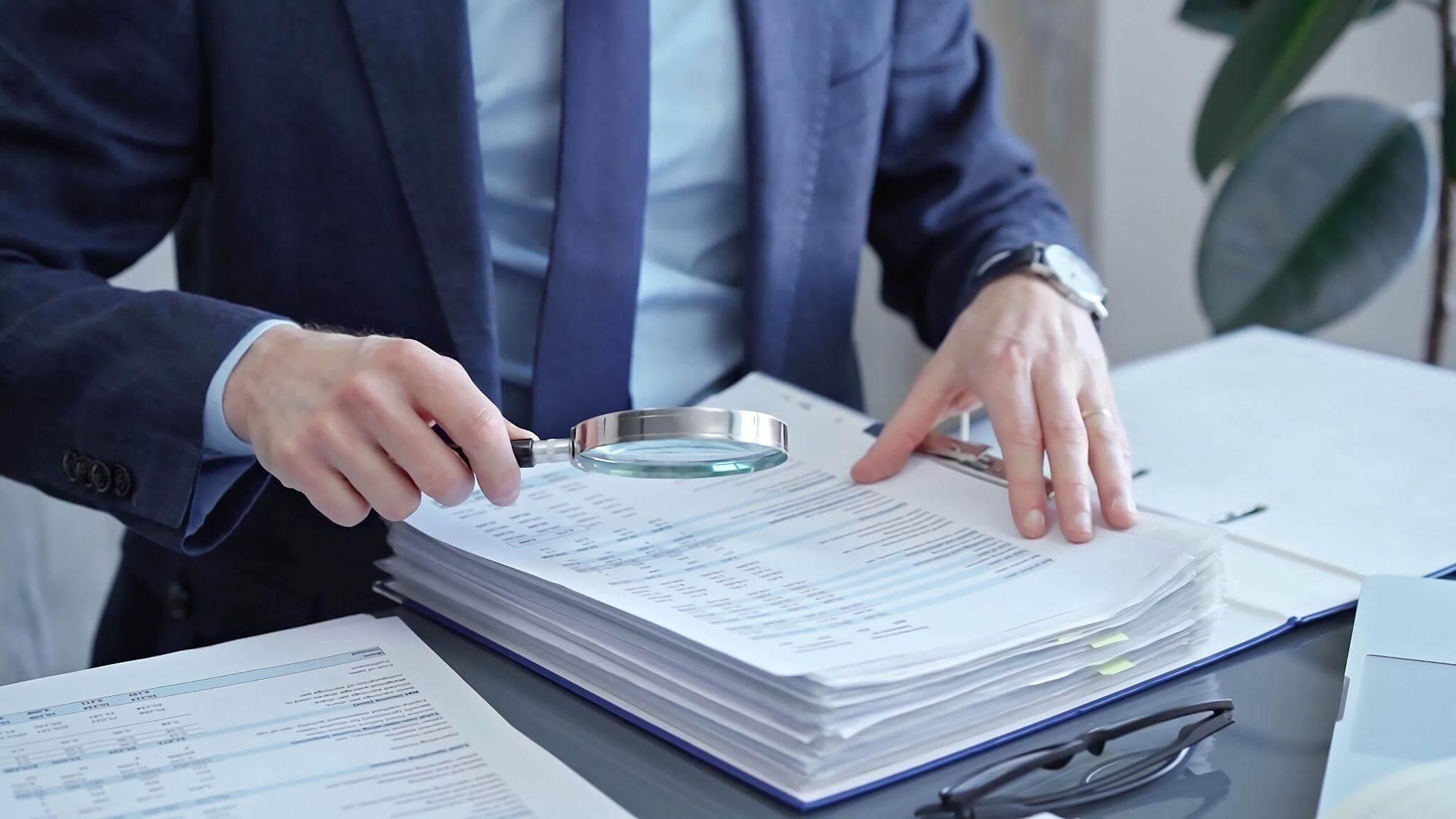 a man holding a magnifying glass over a stack of papers