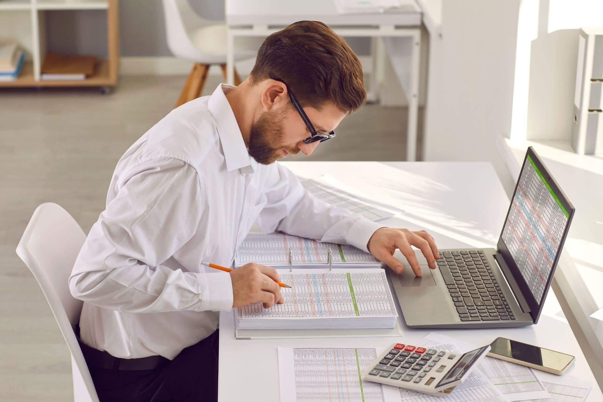 a man sitting at a desk with a laptop and calculator