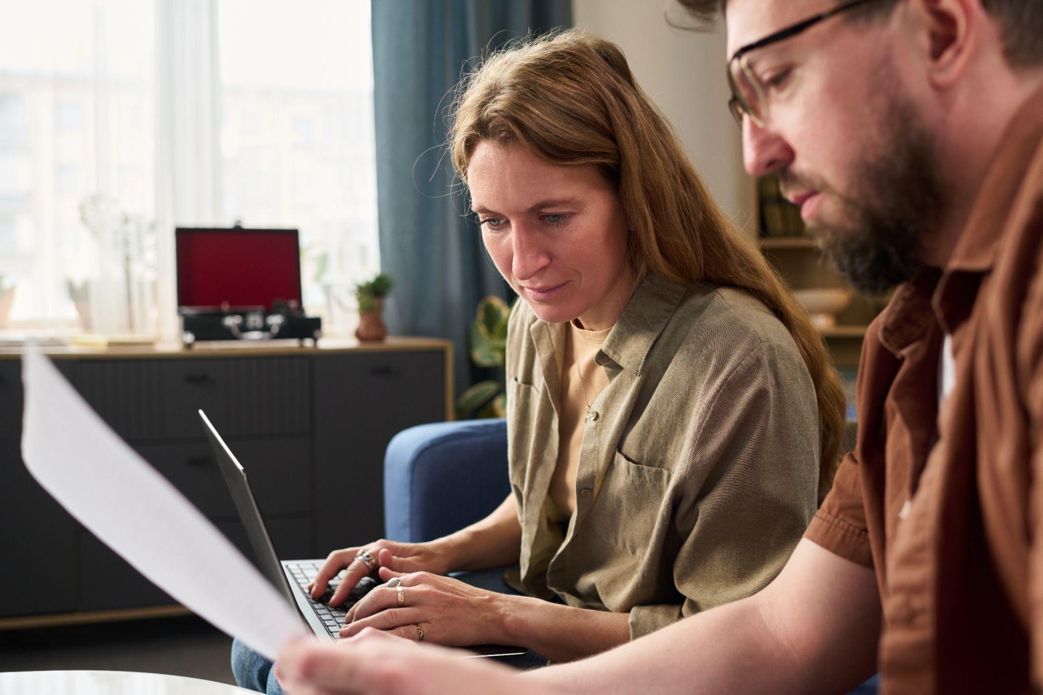 Man and woman collaborating at a laptop and reviewing something in a paper