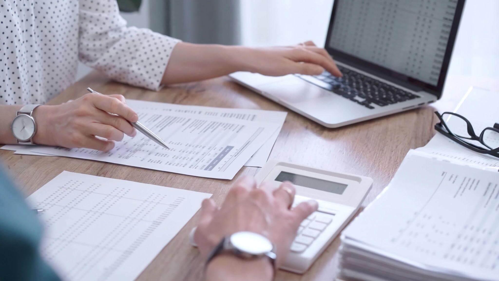 two people sitting at a table with papers and a laptop