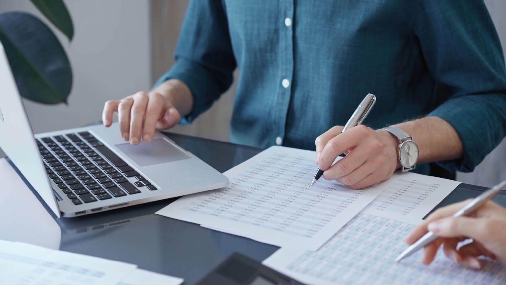 a person sitting at a desk with a laptop and a pen