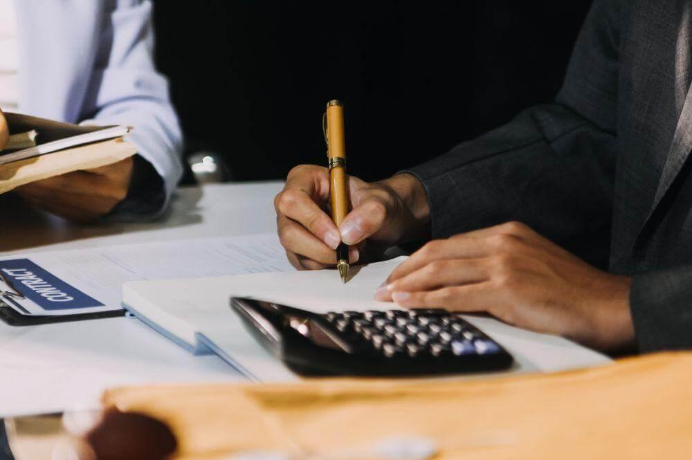 Person writing at a desk, reviewing accounting documents for